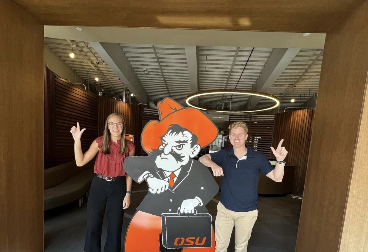 Two students posing with an OSU mascot cutout at an event