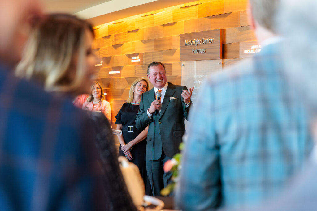 Joe Eastin speaking to an audience during a presentation with Monica Eastin standing beside him